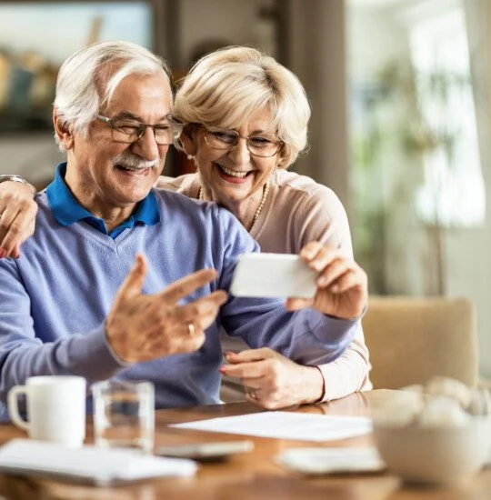 senior couple smile while video calling on their phone at home