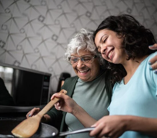 senior woman with her arm around her young granddaughter teaching her to cook