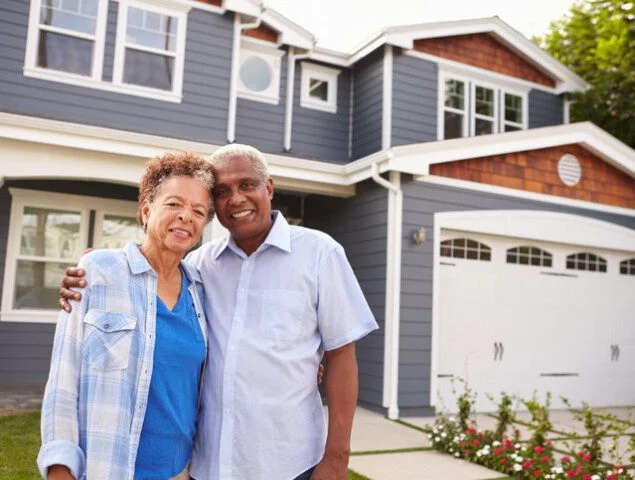 smiling senior couple stands together outside of their home