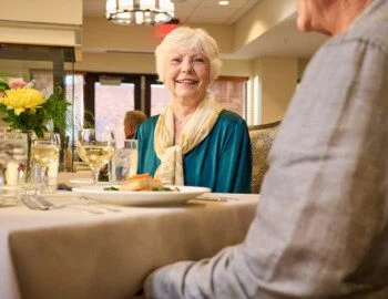 R1 BH Selects R1 (1) Page 02 Image 0010 group of well-dressed senior friends enjoying a meal together in an elegant setting by a glass fireplace