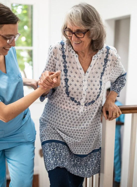 Female caregiver helping senior woman walking up stairs