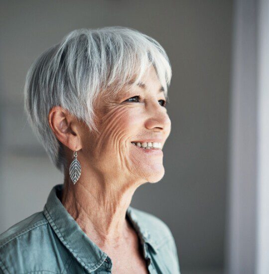smiling senior woman looks out into the distance through her window