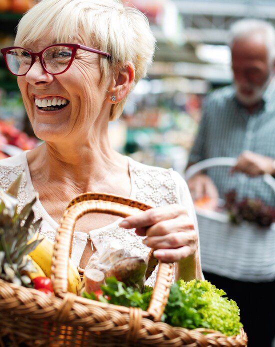 senior woman carries basket of fresh produce at farmers market