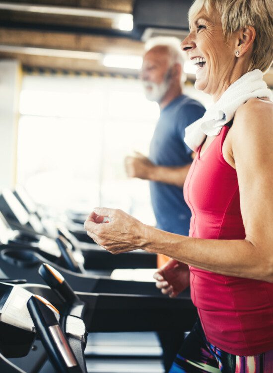 senior woman smiles while walking on the treadmill at her senior fitness center