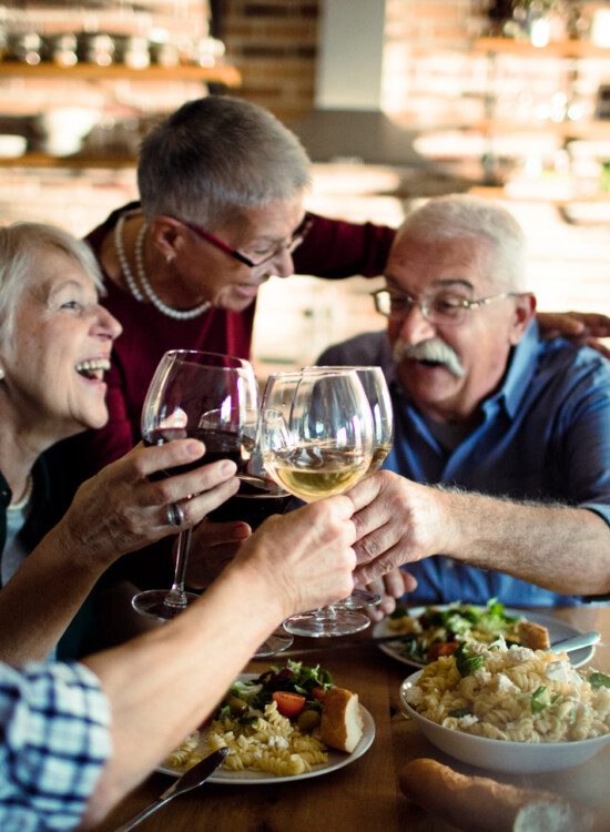 group of senior friends laugh and toast wine glasses over dinner in at elegant venue