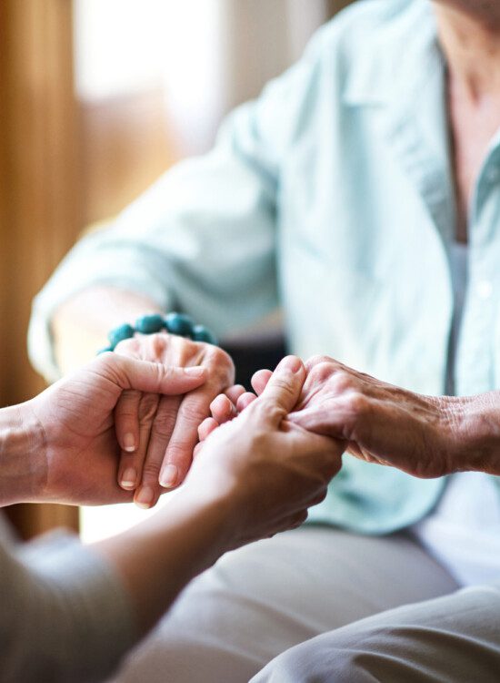 close-up of senior woman seated and holding hands with her adult daughter