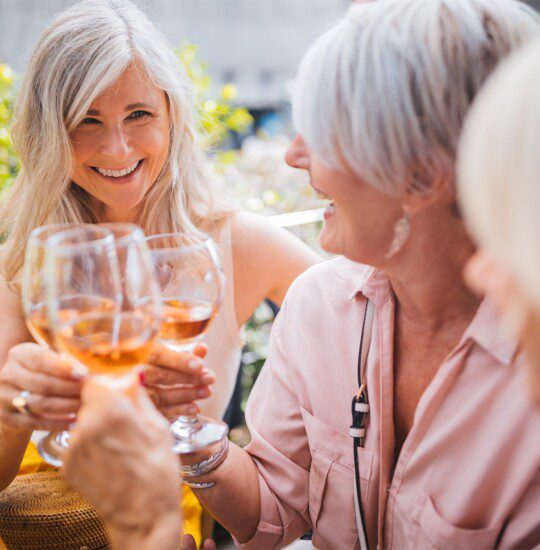 group of senior women laugh and toast wine glasses together