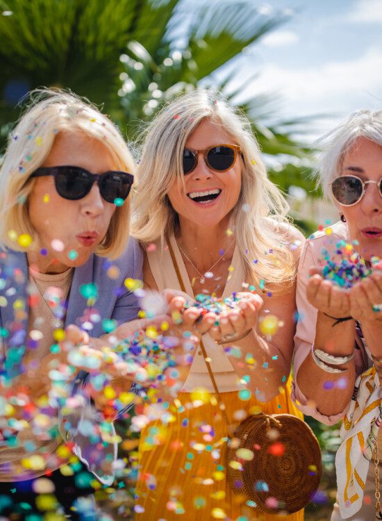 Fashionable senior friends having fun and celebrating by blowing colorful confetti in city street