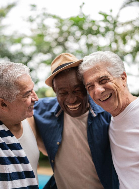 group of three senior men smile and hug outside by a pool