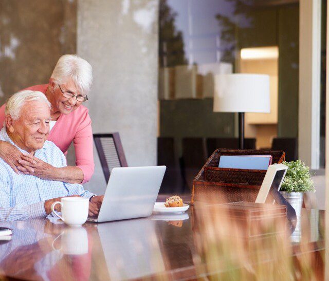 senior couple smiles while video calling loved ones on their laptop