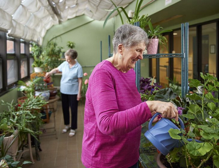 two smiling senior women work on watering the plants in the greenhouse at Beacon Hill Senior Living Community