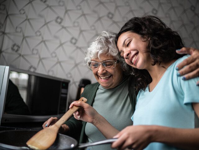 senior woman with her arm around her young granddaughter teaching her to cook