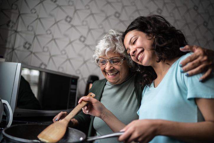 senior woman with her arm around her young granddaughter teaching her to cook