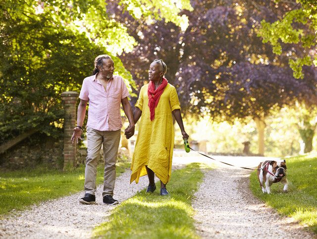 smiling senior couple walks their dog along a beautiful country path surrounded by trees