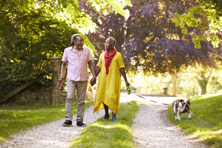 smiling senior couple walks their dog along a beautiful country path surrounded by trees