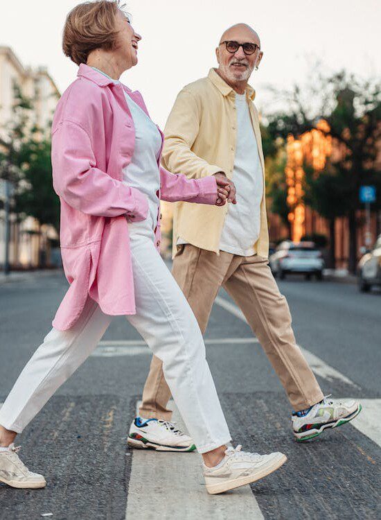 stylish senior man and woman hold hands while crossing the street