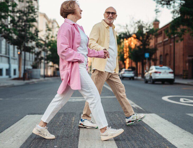 stylish senior man and woman hold hands while crossing the street