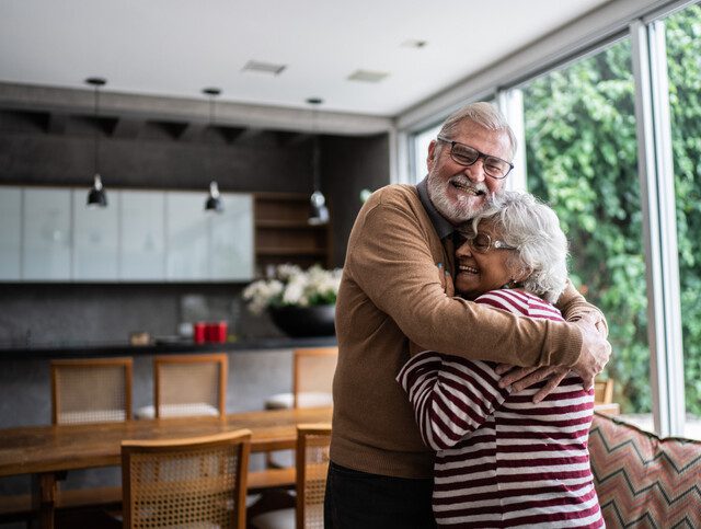 senior couple embrace in a hug inside of their modern home