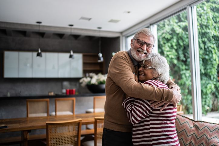 senior couple embrace in a hug inside of their modern home