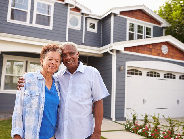 smiling senior couple stands together outside of their home