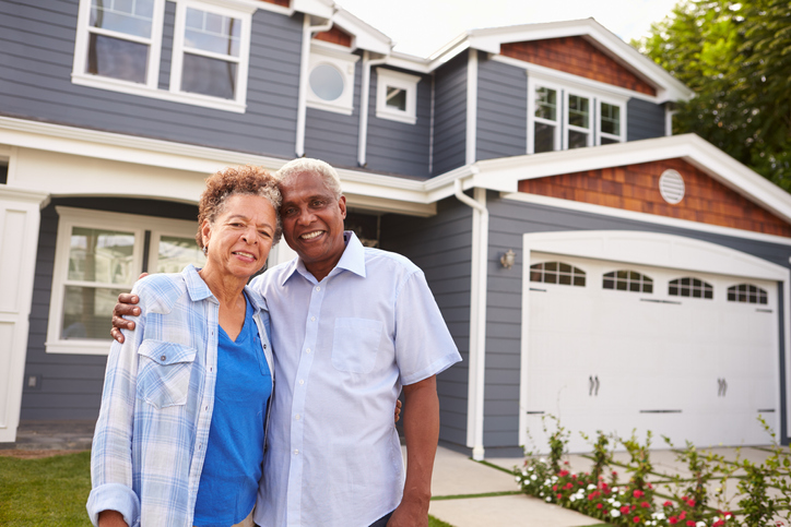 smiling senior couple stands together outside of their home