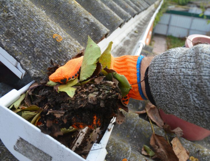 close-up of gloved hand cleaning out debris from a gutter