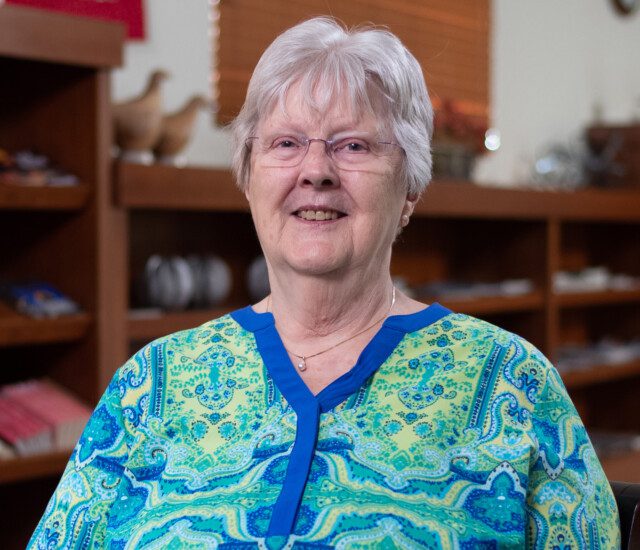 Senior woman (Carol Kaspar) sits in a chair and smiles for an interview