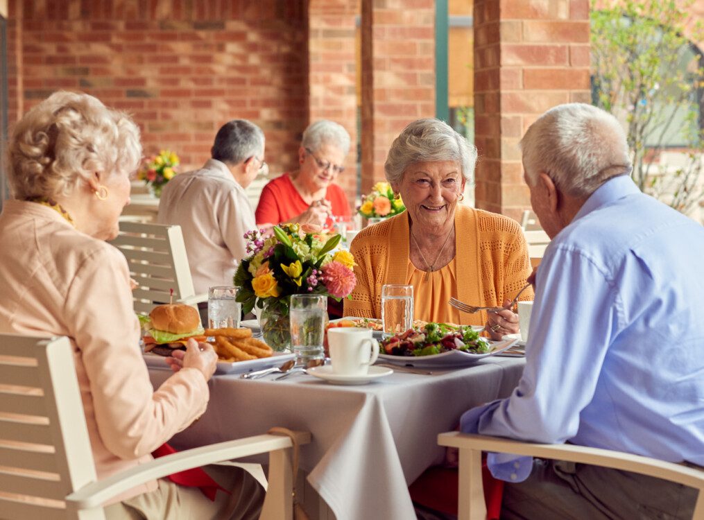 group of well-dressed seniors smile while dining outdoors together and conversing