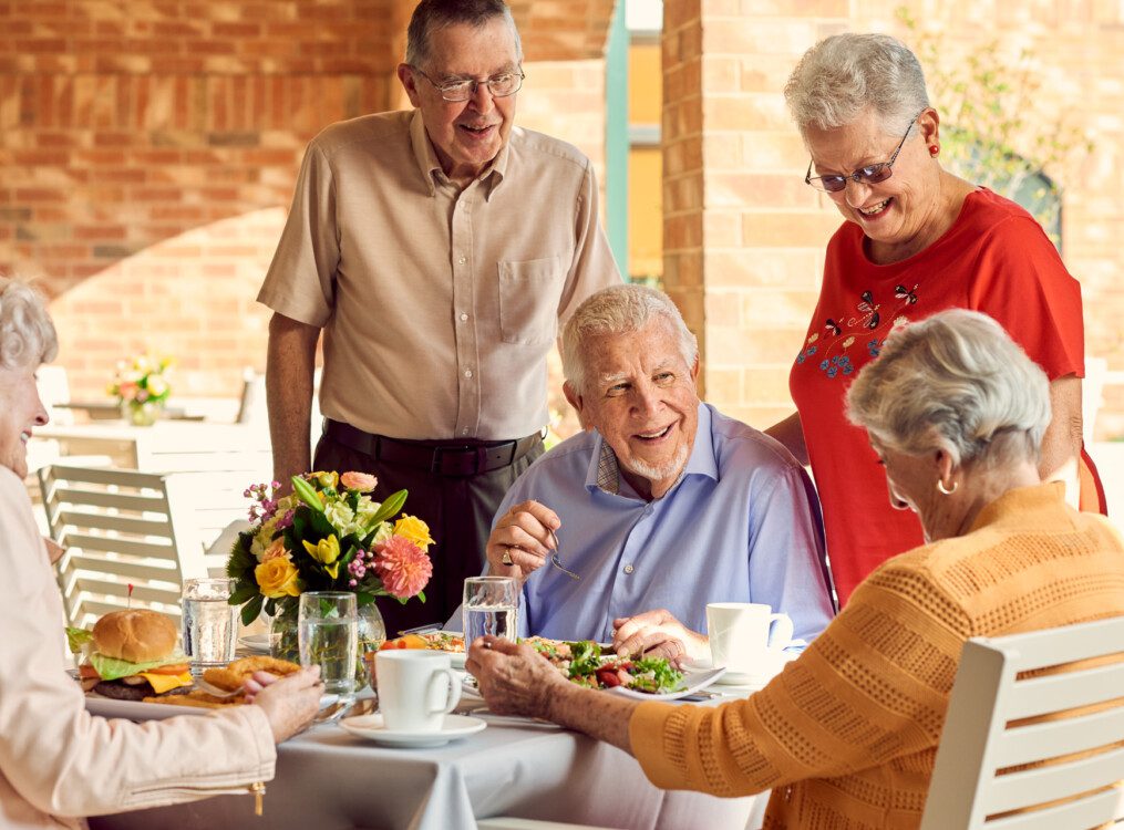 group of well-dressed seniors smile while dining outdoors together and conversing