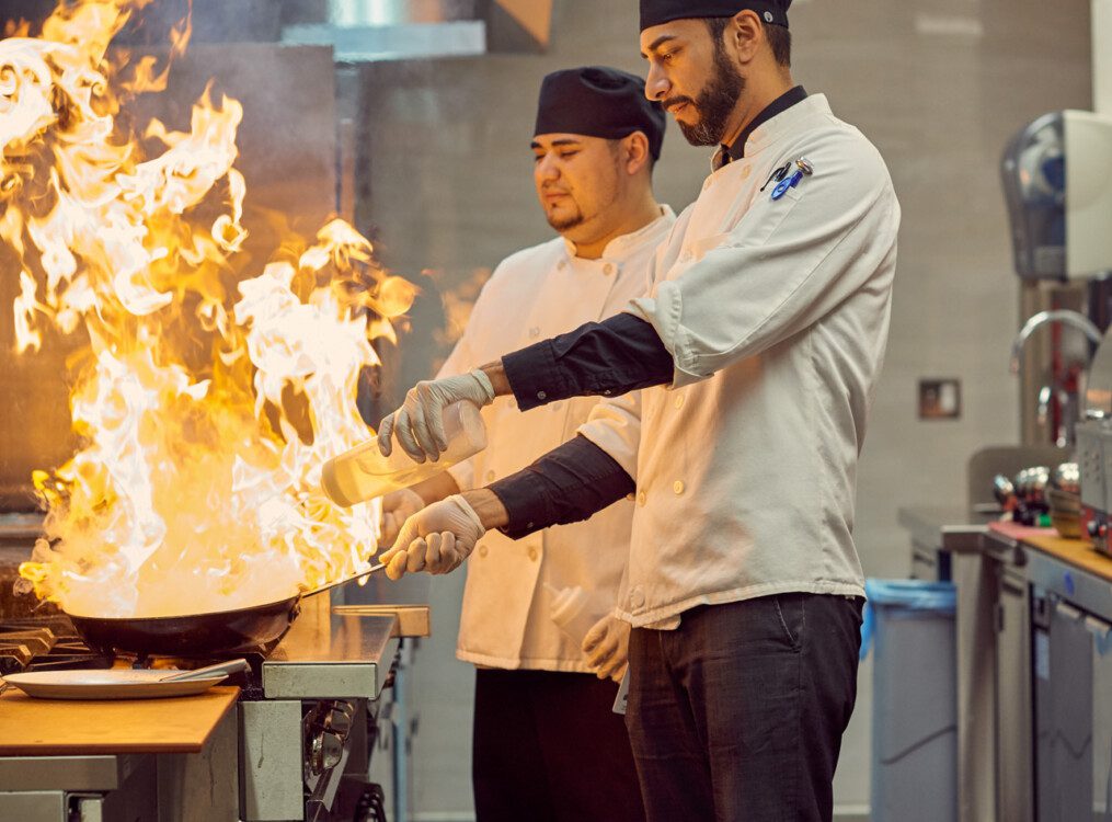 chefs prepare dish in pans, which flame briefly from added alcohol