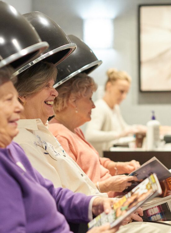 group of senior women smiling and conversing while getting their hair done in the salon at their senior living community