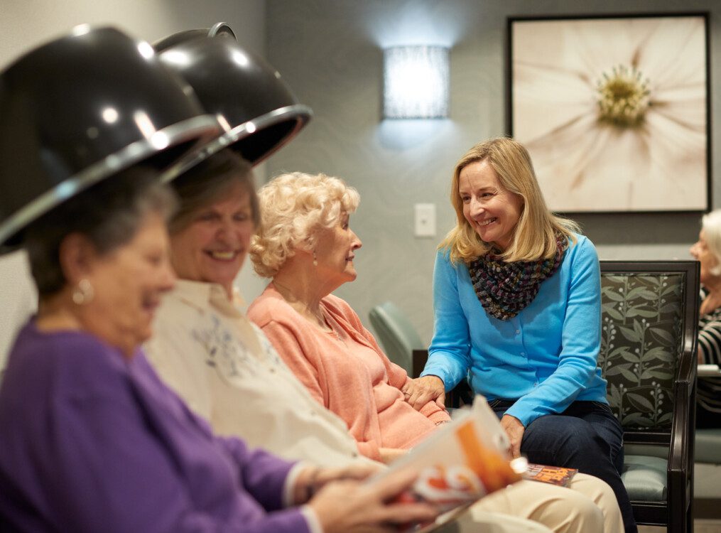 group of senior women smiling and conversing while getting their hair done in the salon at their senior living community