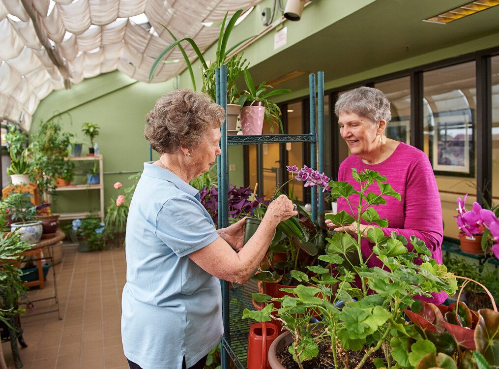 two senior women smile and work in the greenhouse at Beacon Hill Senior Living Community