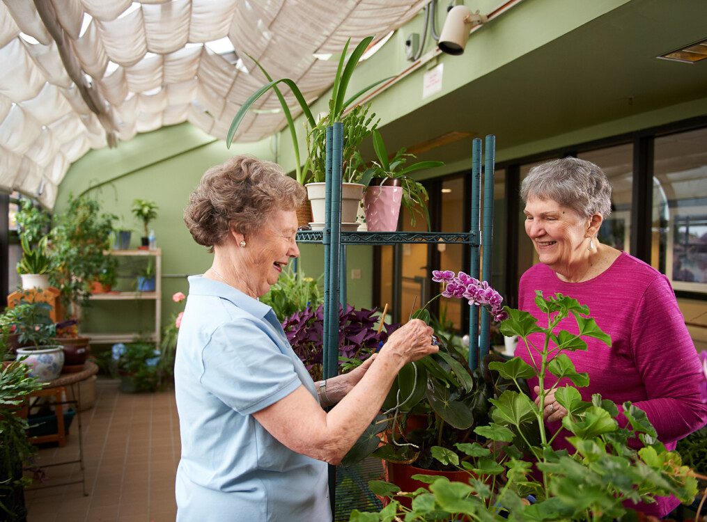two senior women smile and work in the greenhouse at Beacon Hill Senior Living Community