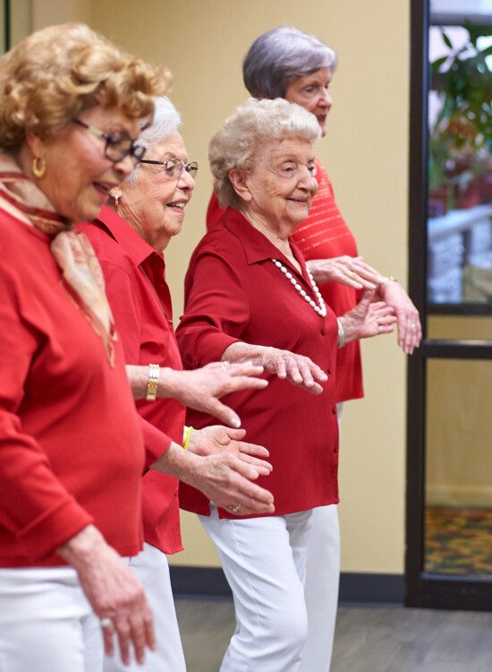 group of senior women in red shirts smile and dance during a class at Beacon Hill Senior Living Community