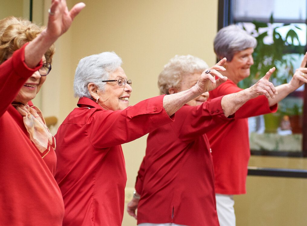 group of senior women in red shirts smile and dance during a class at Beacon Hill Senior Living Community