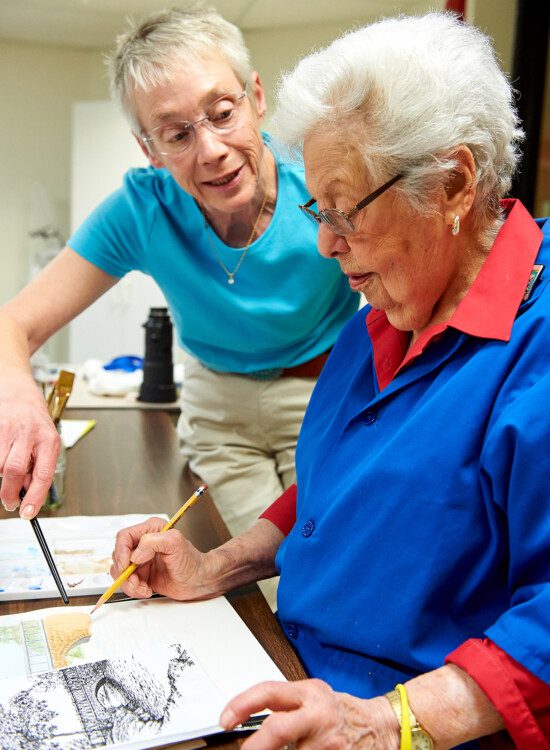 senior woman concentrates on drawing a bridge while receiving tips from the instructor