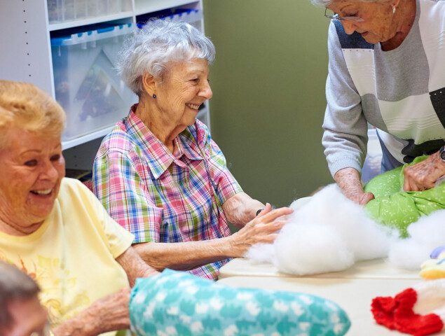 group of senior women smile while working on a crafting project in their senior living community