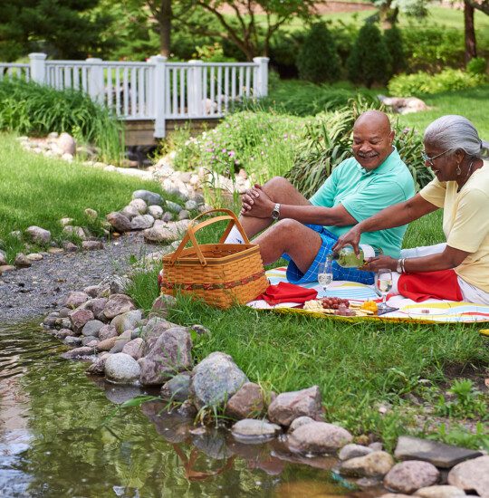 A couple enjoys a picnic by a stream on a sunny day.