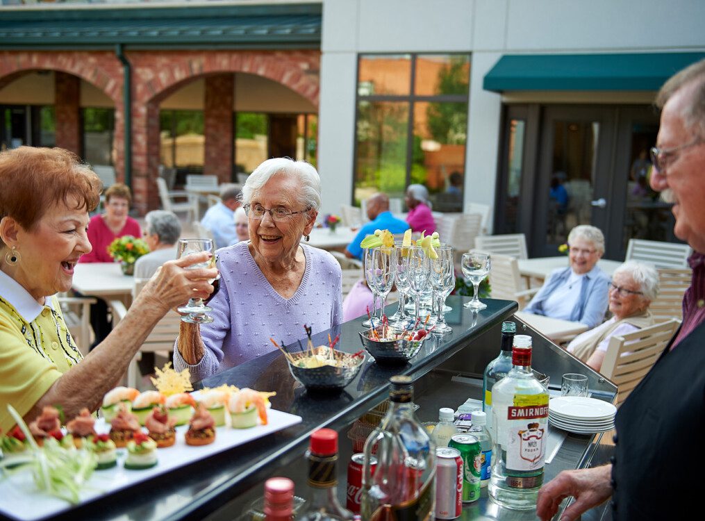 two senior women smile while enjoying cocktails and appetizers at the outdoor lounge and bar at Beacon Hill