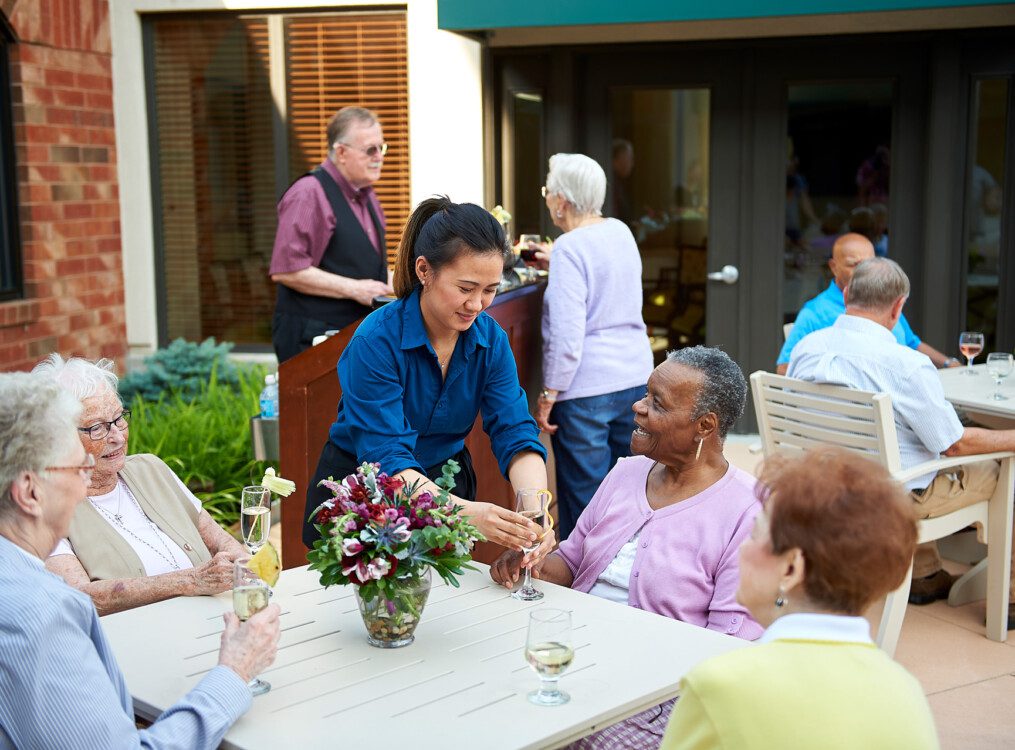 senior woman smiles at waitress filling her wine glass while she dines with friends outdoors