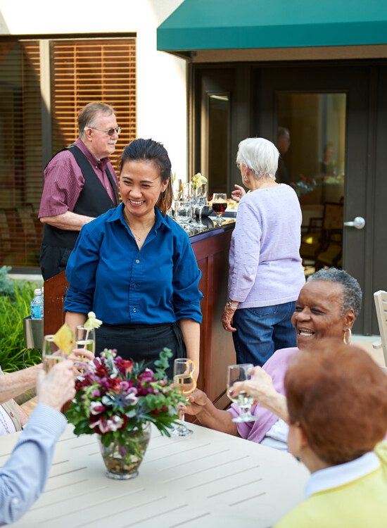 group of happy seniors toast champagne glasses while dining together outdoors at Beacon Hill Senior Living Community