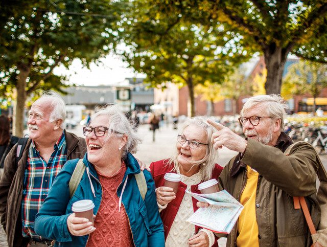 group of senior friends holding coffee smile and point at a landmark while exploring the city