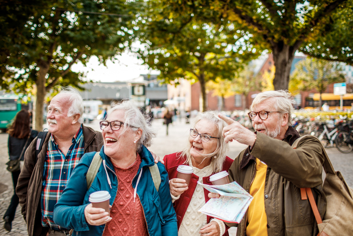 group of senior friends holding coffee smile and point at a landmark while exploring the city
