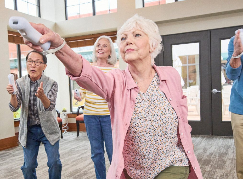 group of senior friends playing Wii games together in the lounge at their senior living community