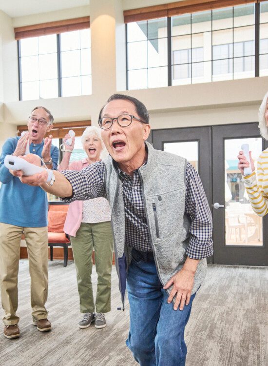 group of senior friends playing Wii games together in the lounge at their senior living community