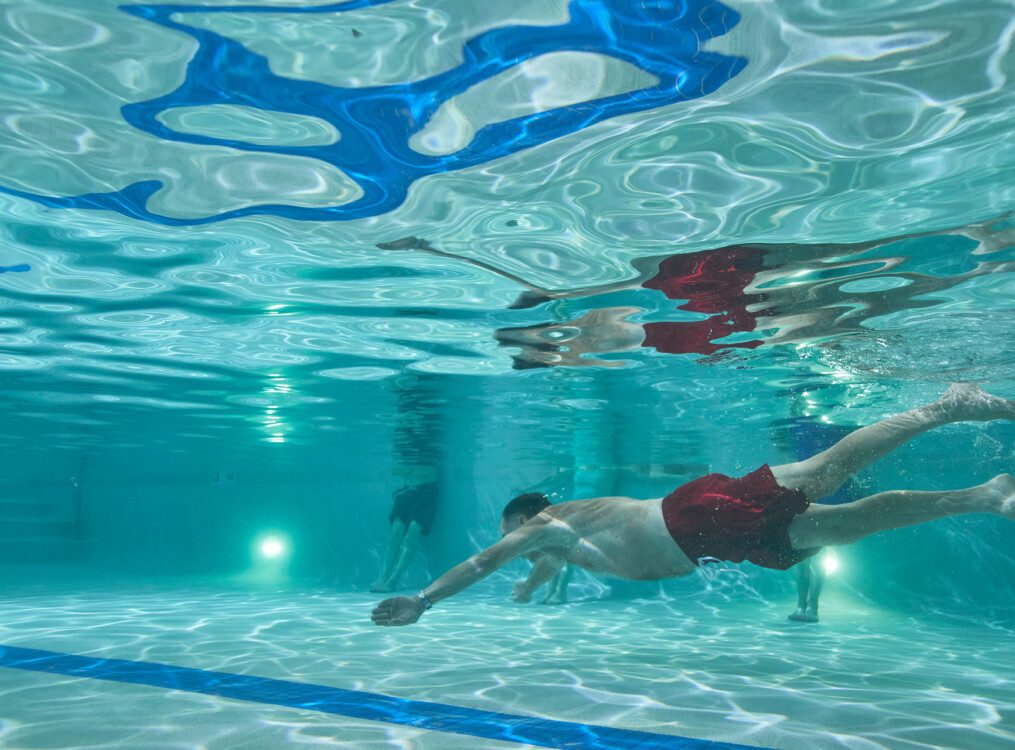 senior man swims underwater in an indoor pool at his senior living community