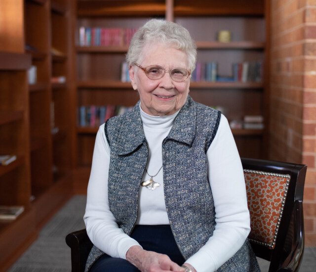 Senior woman (Rita Jenzen) sits in a chair and smiles at the camera for an interview