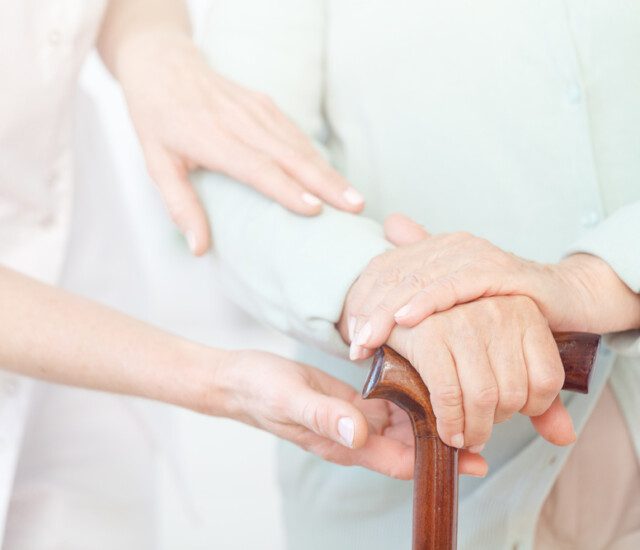 close-up of caregiver's hands gently guiding the arm of a senior man holding a cane