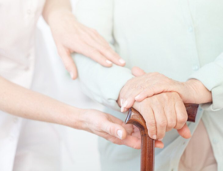 close-up of caregiver's hands gently guiding the arm of a senior man holding a cane